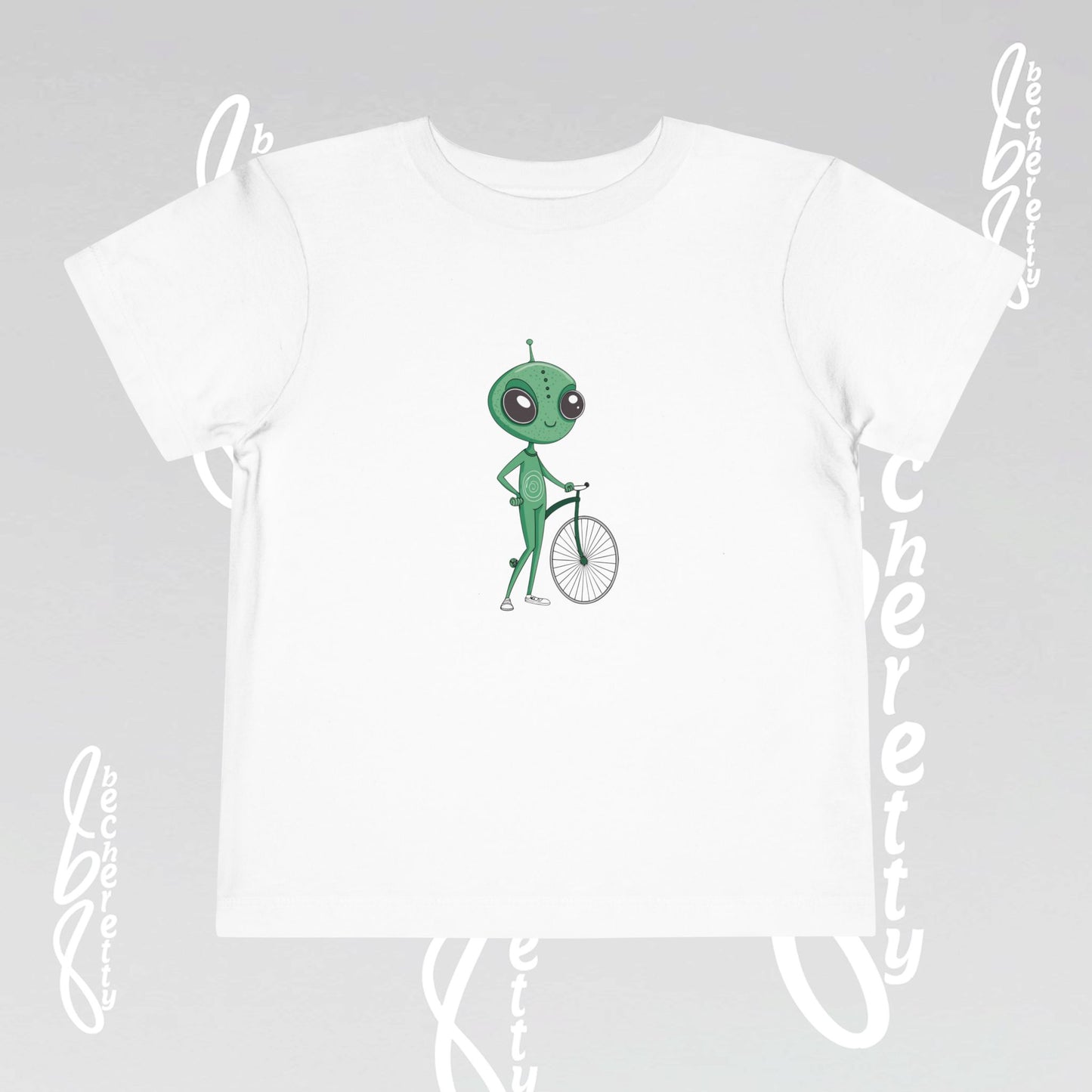 White t-shirt with a green alien on a bicycle graphic on a gray background