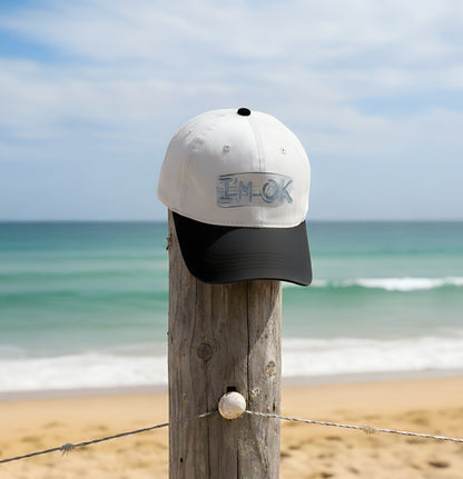 Cap with 'I'm OK' text on a wooden post by the beach