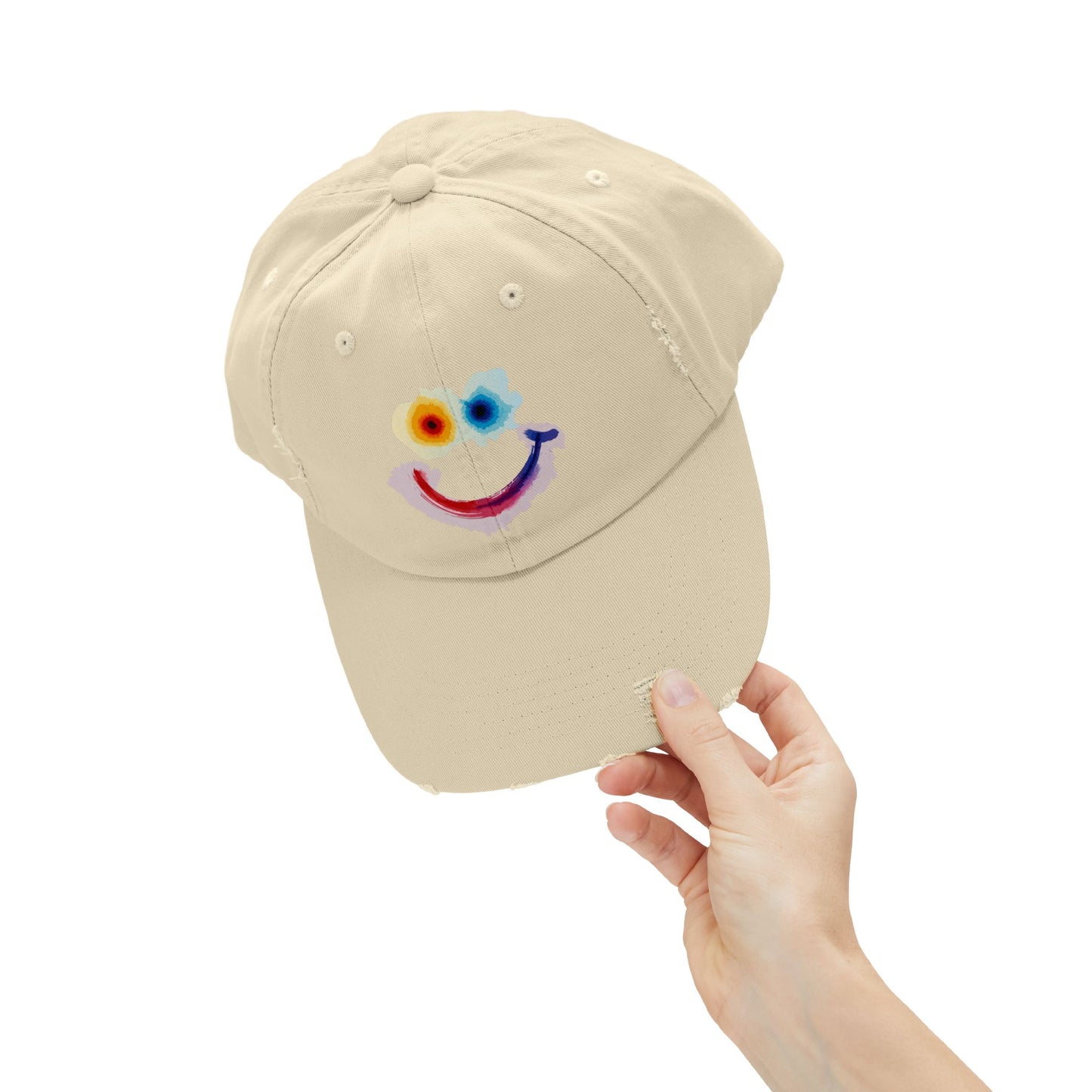 Beige cap with a colorful smiley face design held by a hand on a white background