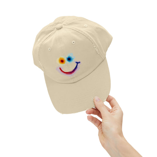 Beige cap with a colorful smiley face design held by a hand on a white background