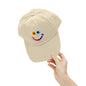 Beige cap with a colorful smiley face design held by a hand on a white background