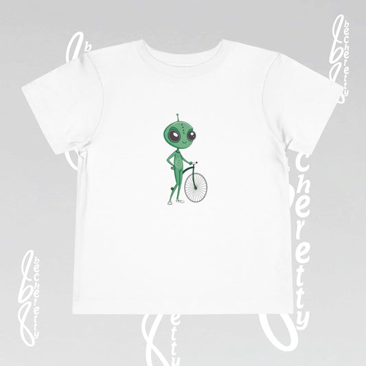 White t-shirt with a green alien on a bicycle graphic on a gray background