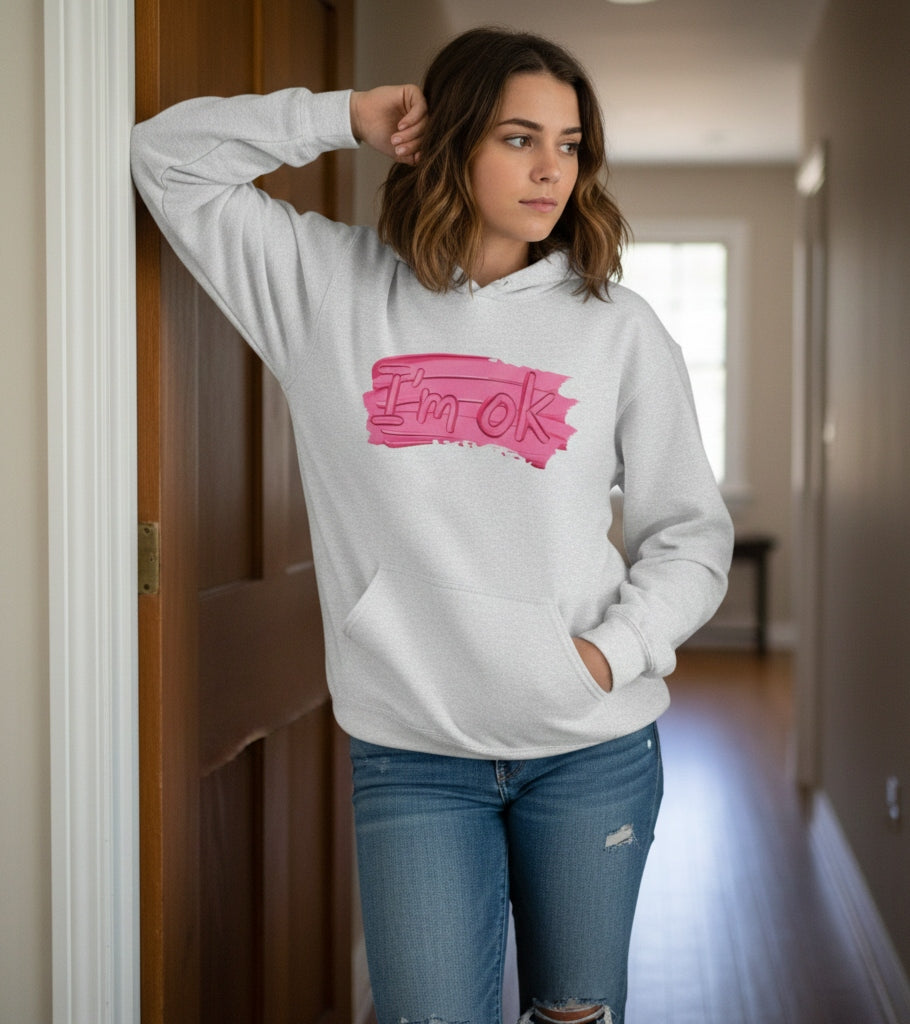 Woman wearing a gray hoodie with a pink graphic and text, standing in a hallway.