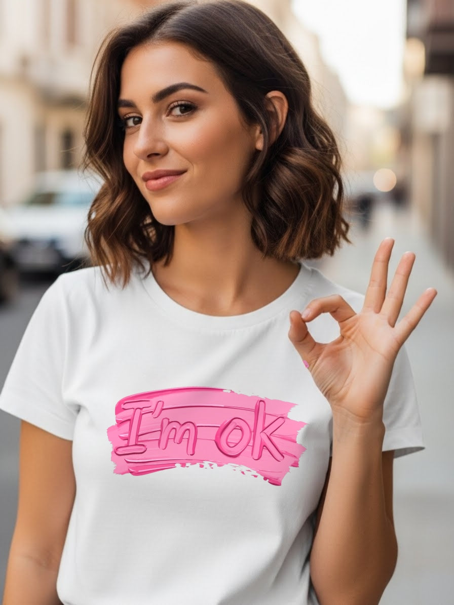 Woman wearing a white t-shirt with 'I'm OK' in pink, making an okay gesture.